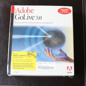 May include: Adobe GoLive 5.0 software box. The box is white with the Adobe logo and product name in red. The box features a graphic of a hand holding a glowing sphere. Includes text: "Professional Web authoring and site management."