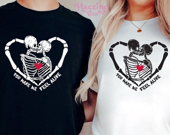 May include: Two black and white skeleton figures holding a red heart, with the text "You make me feel alive" on a black and white t-shirt.