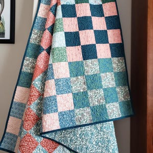 May include: A patchwork quilt featuring a grid of alternating squares in shades of dusty pink, forest green, deep blue, and terracotta, each decorated with intricate floral patterns and finished with a dark blue binding and swirling stitch details.