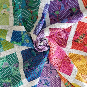May include: A patchwork quilt featuring a variety of square fabric blocks in vibrant shades of green, blue, purple, orange, and yellow. Each block displays floral patterns or polka dots, separated by white sashing with small black polka dots.