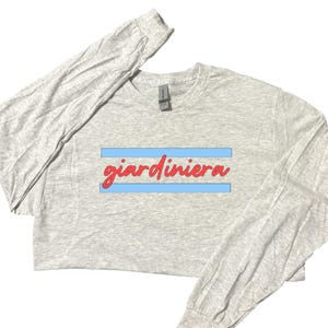 Puede incluir: Una camiseta gris de manga larga con la palabra "giardiniera" impresa en rojo sobre una franja azul.