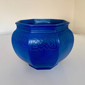 May include: A vibrant cobalt blue ceramic planter. The octagonal planter features embossed Celtic knot patterns. It has a wide opening and a rounded body. Suitable for indoor or outdoor use. The planter is a striking shade of blue.