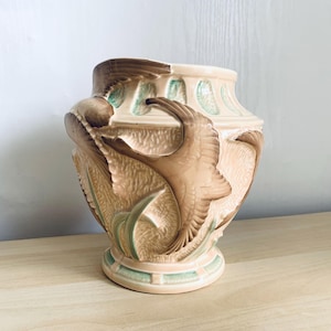 May include: A ceramic vase with a cream-coloured glaze and a brown and green design of stylised birds and leaves.