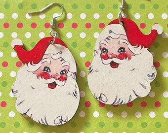 May include: A pair of Christmas-themed earrings featuring a vintage illustration of Santa Claus's face. The earrings are made of wood and have silver hooks.