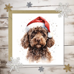 May include: A watercolour illustration of a brown dog wearing a red Santa hat. The dog has brown eyes and a fluffy coat. The image is on a white background with watercolour splatters and is set on a brown card with snowflake decorations.