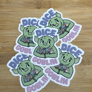 May include: A collection of stickers featuring a green goblin character holding dice. The stickers have the words "DICE" and "GOBLIN" in a playful font. The background is a light brown wood grain.