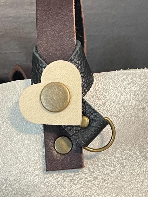 Flair holder to safely attach charms to PLG Portland Leather Goods bags. Made with pebble black and Bone full grain leather. Bronze hardware