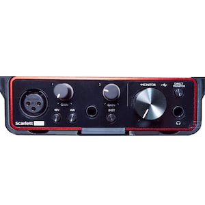 Puede incluir: Una interfaz de audio Focusrite Scarlett Solo de 3.ª generación negra con detalles rojos. Tiene una entrada XLR única con un interruptor de alimentación fantasma de 48 V, una perilla de ganancia, un botón de aire, una entrada de instrumento de 1/4 de pulgada con una perilla de ganancia, un botón de inst, una perilla de monitor, un botón de monitor directo y una toma de auriculares de 1/4 de pulgada.