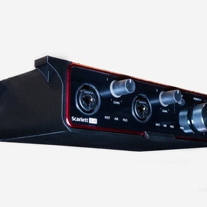 Pode incluir: Uma interface de áudio Focusrite Scarlett 4i4 preta e vermelha com duas entradas de microfone, duas entradas de instrumento e um botão de monitor.