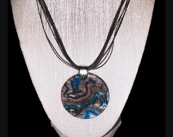 Puede incluir: Un collar de múltiples hilos con un colgante redondo que presenta un diseño abstracto en espiral en tonos azules, marrones y dorados.