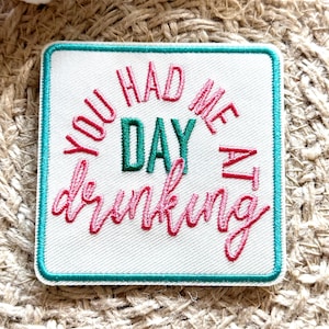 Op de afbeelding: Witte geborduurde patch met een turquoise rand. De tekst luidt "You had me at day drinking" in roze en groene letters.