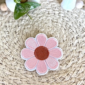 May include: A pink and brown embroidered flower patch. The flower has a brown center and pink petals.