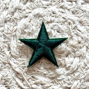 May include: A dark green embroidered star patch. The star is five-pointed and has a slightly textured surface.