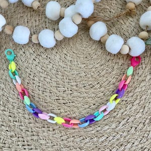 May include: A colourful plastic chain necklace with alternating links in pink, purple, yellow, blue, green and white.