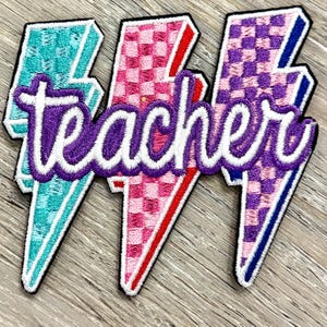 Puede incluir: Tres parches bordados con forma de relámpagos. Cada rayo tiene un color y un patrón diferente: turquesa, rosa y morado. La palabra "teacher" está bordada en escritura morada sobre los rayos.
