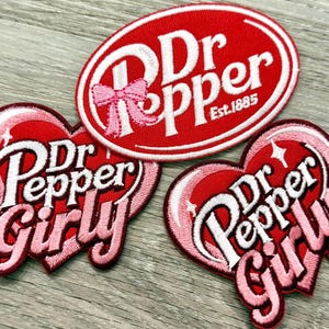 Puede incluir: Tres parches bordados con el logo de Dr Pepper. Uno es de forma ovalada con el texto "Dr Pepper Est. 1885" en blanco sobre fondo rojo. Dos parches en forma de coraz&oacute;n dicen "Dr Pepper Girly" en blanco y rosa.