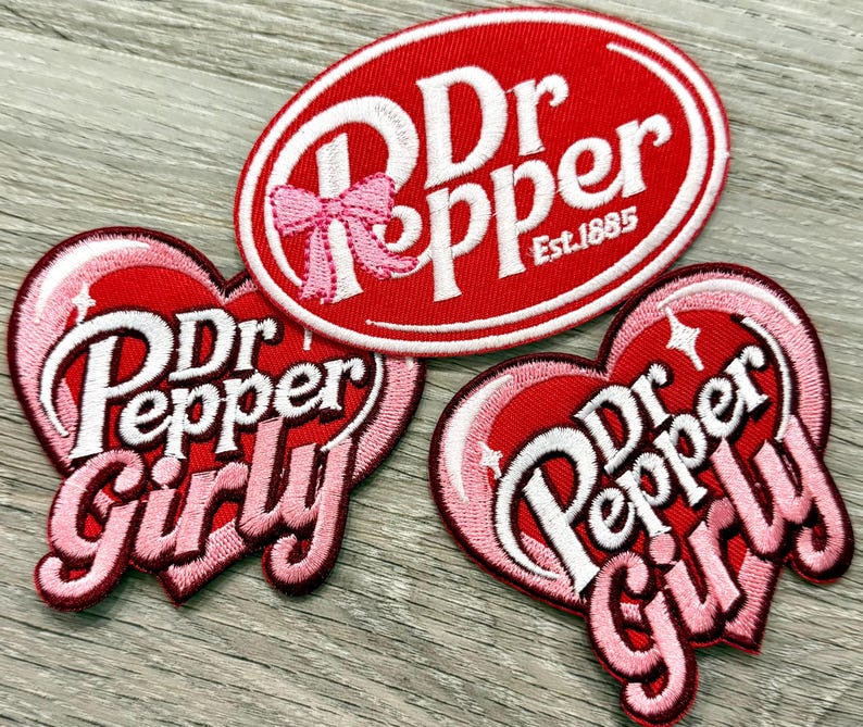 Puede incluir: Tres parches bordados con el logo de Dr Pepper. Uno es de forma ovalada con el texto "Dr Pepper Est. 1885" en blanco sobre fondo rojo. Dos parches en forma de coraz&oacute;n dicen "Dr Pepper Girly" en blanco y rosa.