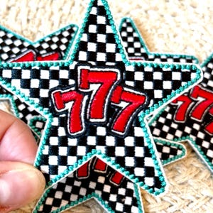Peut inclure: Écusson en forme d'étoile avec un motif à carreaux noir et blanc. Le chiffre "777" est affiché en rouge, souligné de blanc. L'écusson a une bordure turquoise. Plusieurs écussons sont visibles.