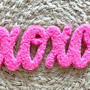 May include: Pink fluffy felt letters spelling out "XOXO" on a woven background.