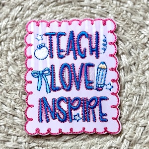 Peut inclure: Un écusson rectangulaire rose et blanc avec les mots "TEACH LOVE INSPIRE" brodés en bleu. L'écusson a un bord festonné avec des coutures roses et comprend de petites images brodées d'une pomme, d'un crayon, d'un nœud et d'étoiles.