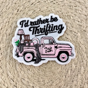 May include: An embroidered patch featuring a light pink pickup truck carrying furniture and the text I'd rather be Thrifting in black script. The truck door has the words Thrift Queen embroidered in black thread on the side panel.