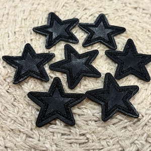 May include: Seven black felt star-shaped patches with a black outline. The patches are on a woven beige background.