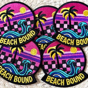 May include: A collection of embroidered patches with a retro beach theme. Each patch features a palm tree, waves, and a setting sun against a pink and purple sky. The words "BEACH BOUND" are embroidered in yellow.