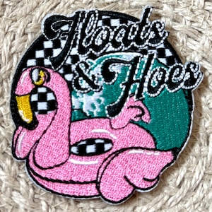 以下が含まれることがあります： ピンクのフラミンゴの浮き輪のデザインと「Floats & Hoes」の文字が刺繍されたパッチ。パッチは白と黒のチェック柄、緑色の背景、黒い縁取りが特徴です。