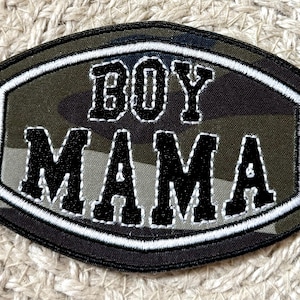 Può includere: Toppa ricamata in bianco e nero con le parole "BOY MAMA" in un carattere audace e squadrato. La toppa ha uno sfondo mimetico nei toni del verde, marrone e grigio e un bordo bianco.