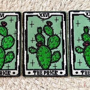 May include: Three rectangular embroidered patches. Each patch features a green cactus with pink flowers on a light green background. The patches have the Roman numeral XXVI at the top and the words "THE PRICK" at the bottom, with a black border.