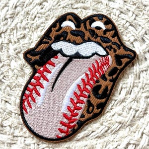 May include: Embroidered patch depicting lips with a baseball tongue. The lips have a brown and black leopard print design. The tongue is a baseball with red stitching and a white stripe.