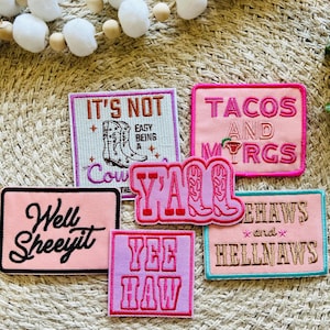 以下が含まれることがあります： 「It's Not Easy Being a Cow」「Tacos and Margaritas」「Y'all」「Yee Haw」「Yeehaws and Hellnaws」「Well Sheeyit」など、さまざまな言葉が書かれたピンクとパープルの刺繍入りアイロン接着パッチ6枚。