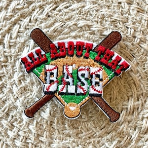 May include: Embroidered patch featuring a baseball diamond design with crossed bats. The patch has the text "ALL ABOUT THAT BASE" in red and white, with a green and brown color scheme. The patch is on a woven background.