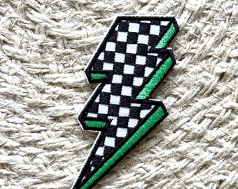 Pode incluir: Um remendo de raio preto e branco xadrez com contorno verde. O remendo é feito de tecido e tem um design costurado.