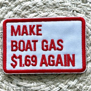 May include: Embroidered patch with a white background and red border. The patch reads "MAKE BOAT GAS $1.69 AGAIN" in red, bold letters. The patch is rectangular and sits on a textured, neutral-coloured surface.