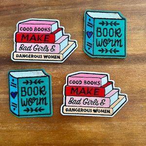 Könnte beinhalten: Vier gestickte Aufnäher mit Buchmotiven. Zwei Aufnäher zeigen Bücherstapel mit dem Text "GOOD BOOKS MAKE Bad Girls & DANGEROUS WOMEN". Die anderen beiden Aufnäher sagen "BOOK WORM".