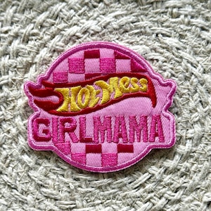 May include: A pink embroidered patch featuring the Hot Wheels logo in yellow and red, and the text "GIRLMAMA" in pink. The patch has a checkered pattern background.