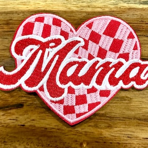 Op de afbeelding: Rood en wit geruit hartvormig patch met het woord "Mama" geborduurd in wit op een rode achtergrond.