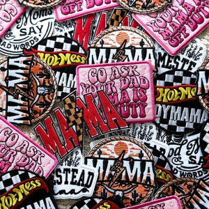 Può includere: Una collezione di toppe ricamate colorate con la parola "Mama" in vari stili e design. Alcune toppe hanno uno sfondo a scacchi, mentre altre presentano una scena di tramonto con cactus e un cappello da cowboy. Il testo "Go Ask Your Dad Mama Is Off Duty" è ripetuto su diverse toppe.