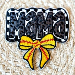 Puede incluir: Parche de tela a cuadros blanco y negro con la palabra "Mama" en negro y un lazo de softball amarillo y rojo.