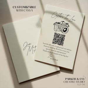 Peut inclure: Deux cartons de mariage blanc cassé avec du texte noir. L'un des cartons porte une illustration d'appareil photo et un code QR, avec le texte "Capture the Love". L'autre carton porte les noms "Jen & Mitch". Les cartons sont de Parker & Co. Creative Studio.