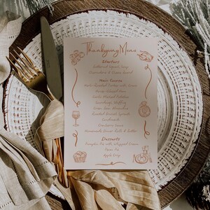 May include: Thanksgiving menu card on a white plate with gold silverware. The menu lists starters, main course, and desserts. The card is decorated with illustrations of food and drink.