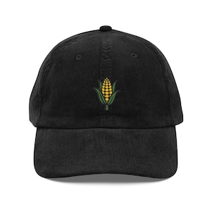 May include: Black corduroy baseball cap featuring an embroidered corn graphic in yellow and green. The cap has a curved brim and an adjustable strap for a comfortable fit. A stylish accessory for casual wear.