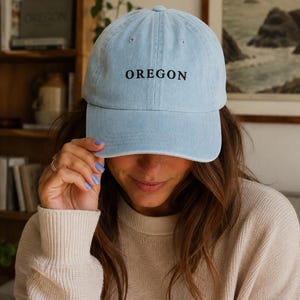 Op de afbeelding: Een lichtblauwe baseballpet met een gebogen klep en een gestructureerde kroon. Het woord OREGON is in zwarte hoofdletters in het midden op de voorkant geborduurd. De pet is voorzien van bijpassende lichtblauwe stiksels en kleine ventilatiegaatjes.