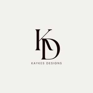 以下が含まれることがあります： ダークブラウンで「K」と「D」の文字が組み合わされたミニマリストロゴデザイン。文字の下には、「KAYKES DESIGNS」のテキストが、ニュートラルな背景に対して、すっきりとしたサンセリフ体で表示されています。
