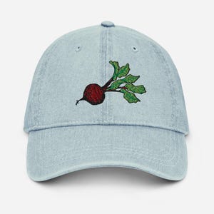 Puede incluir: Gorra de béisbol de mezclilla azul claro con un bordado de un diseño de remolacha roja con hojas verdes. La gorra tiene una visera curva y un diseño clásico de seis paneles. Un accesorio casual.