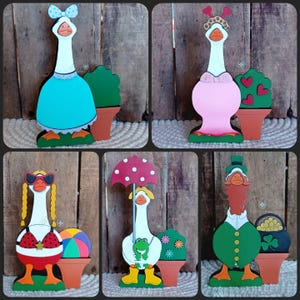 May include: Set of six wooden goose figurines, each with a different theme and outfit. The geese are painted in various colors, including blue, pink, red, green, and white. Each goose is holding a different accessory, such as an umbrella, a beach ball, a pot of gold, a frog, and a heart-shaped bush.