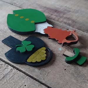 May include: A set of wooden cutouts for a leprechaun, pot of gold, and shamrock. The leprechaun is wearing a green hat and coat, and the pot of gold is filled with gold coins. The shamrock is green.
