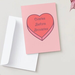 May include: A pink card with a red heart-shaped candy illustration. The candy has the text "Ovaries Before Brovaries" written on it.