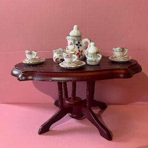 May include: A miniature porcelain tea set with a floral design on a dark wood table. The set includes a teapot, creamer, sugar bowl, and four teacups and saucers.